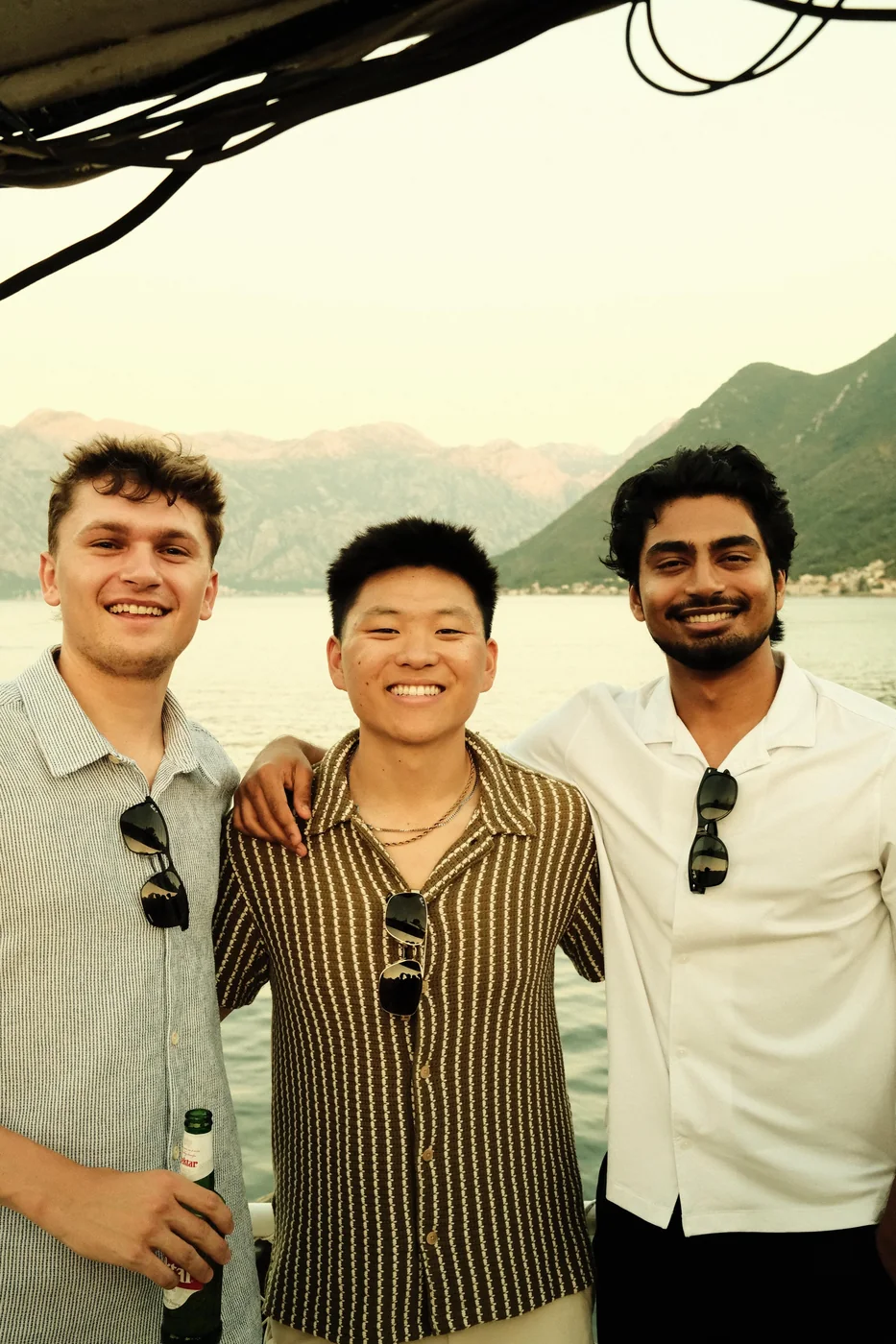 Nate Herk with two friends on a boat in Montenegro, mountains behind them.