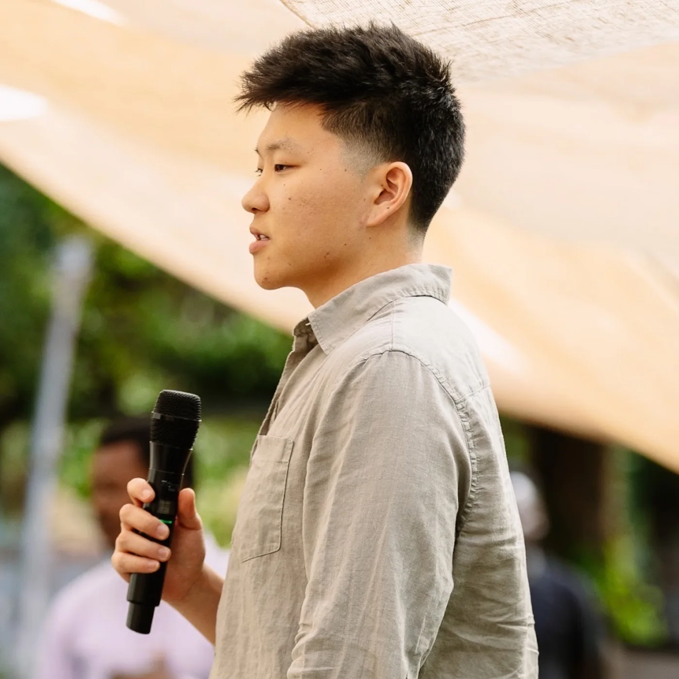 Nate Herk speaking into a microphone at an outdoor event.